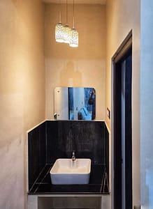 A small washbasin area with a white sink set on a black countertop, a wall-mounted mirror above, and three decorative hanging lights overhead.
