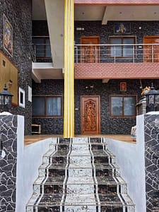 Exterior with black stone walls, a carved wooden door, tiled stairs, and a yellow-and-white pillar at the entrance.